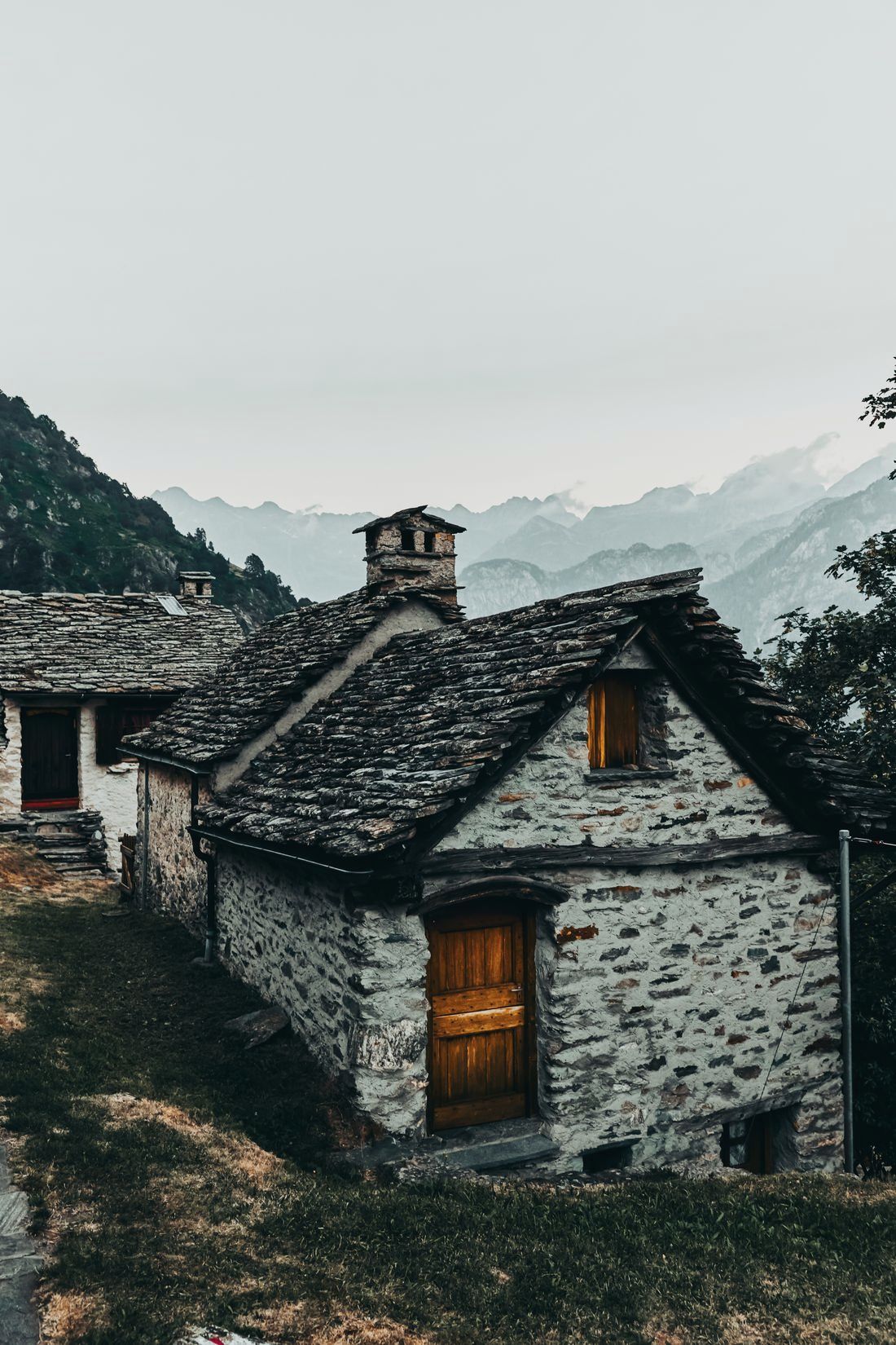 Restored stone farmhouse with a stone-slab roof on a wooded mountain slope